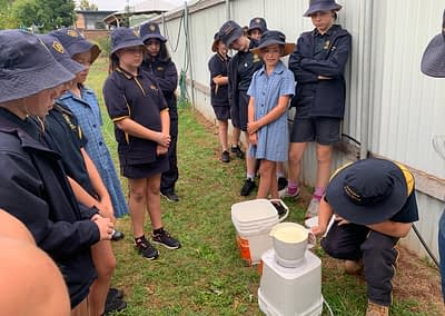 students watching a student mix milk powder in a white bucket